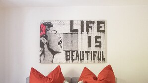 Een slaapkamer met een bed, rode en witte kussens en een kunstwerk met een citaat.