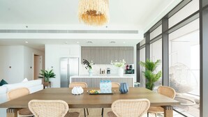A modern dining area with a wooden table, wicker chairs, and a hanging light fixture. - KeyRock - Sea View Beachfront Penthouse (Dubai)