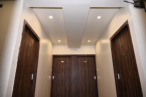 A modern bathroom with wooden doors, recessed ceiling lights, and a white tiled wall. - Atharv Kaashi - Behind Sigra Sports Stadium (Varanasi)