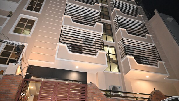 A multi-story building with a modern design, featuring balconies with metal railings and a brick entrance. - Atharv Kaashi - Behind Sigra Sports Stadium (Varanasi)