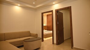 A modern hotel room with a sofa, a round coffee table, a ceiling fan, recessed lighting, and a wooden wardrobe. - Atharv Kaashi - Behind Sigra Sports Stadium (Varanasi)