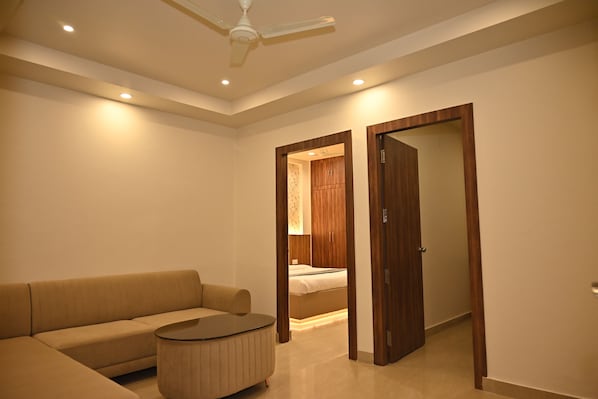 A modern hotel room with a sofa, a round coffee table, a ceiling fan, recessed lighting, and a wooden wardrobe. - Atharv Kaashi - Behind Sigra Sports Stadium (Varanasi)
