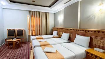 A hotel room with three beds, a TV, and a desk.