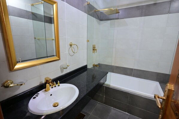 A bathroom with a white sink, gold fixtures, a glass shower enclosure, and a bathtub. - Rahaf Al Mashaer Hotel (Makkah)