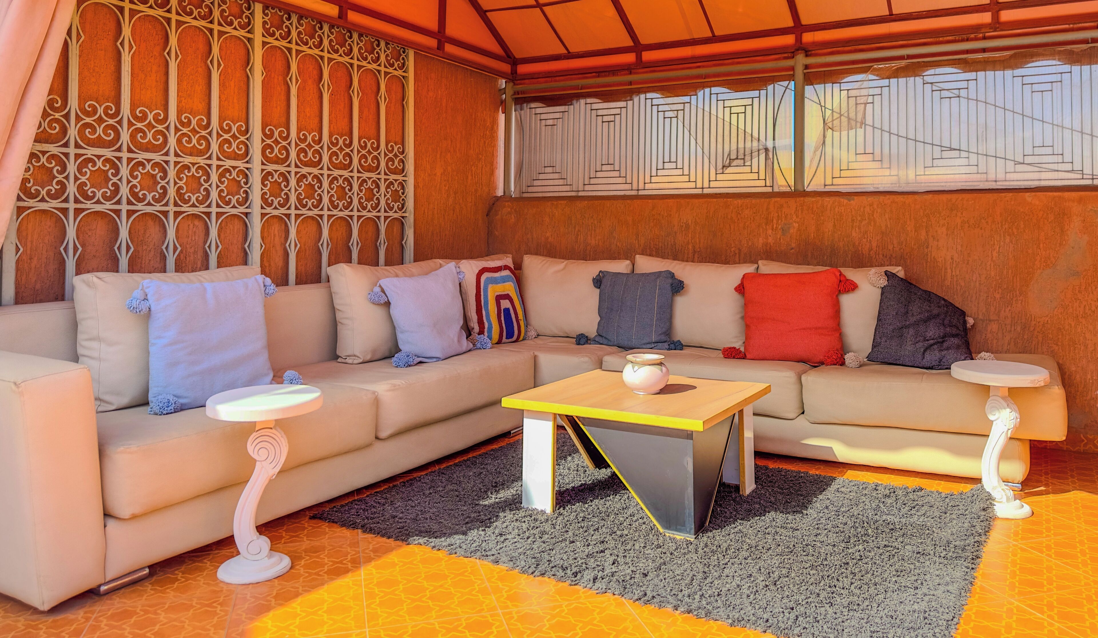 Una sala de estar moderna con un sofá color beige, almohadas de colores, una mesa de centro de madera y una alfombra estampada.