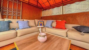 Een moderne woonkamer met een beige modulaire bank, een roze vaas op een houten salontafel en een wand met een geometrisch patroon.