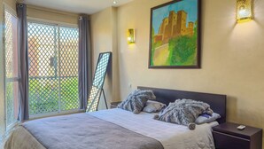 Een slaapkamer met een bed, nachtkastjes, een schilderij en een raam met uitzicht.