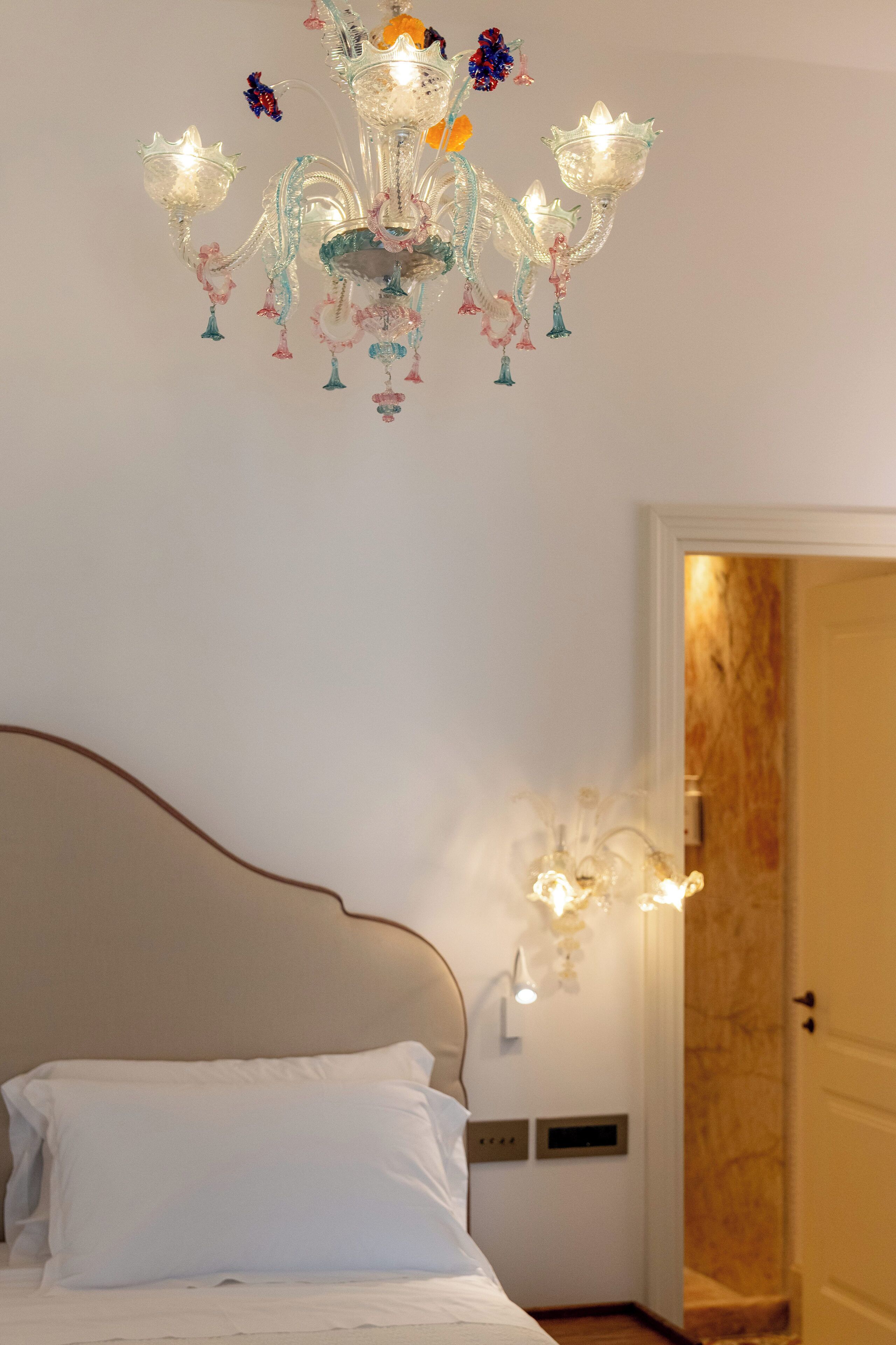 A bedroom with a bed, a chandelier, and a wall-mounted light fixture.