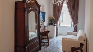 Una habitación con un armario de madera, un sofá blanco, una mesa de comedor con sillas, una araña y una ventana con cortinas.