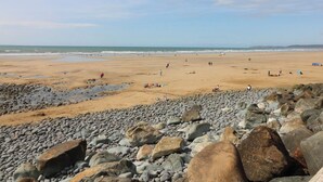 Une plage de galets et de rochers au premier plan, une plage de sable au milieu, et l’océan à l’arrière-plan.