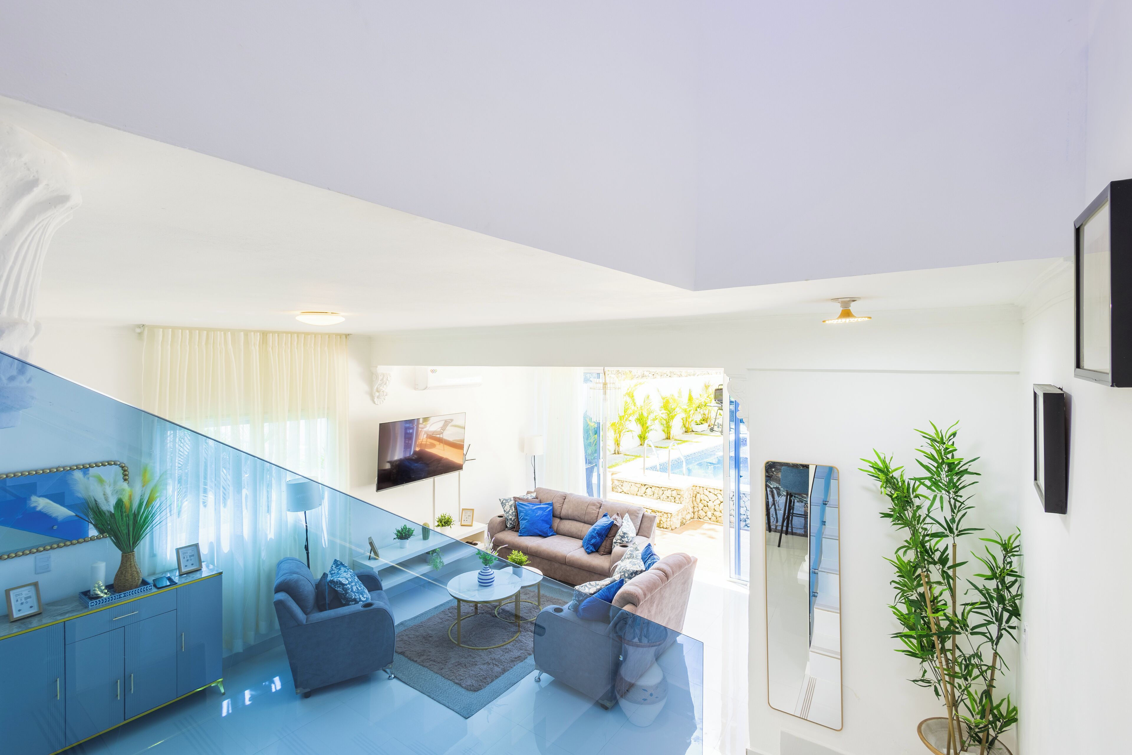 A modern living room with a sofa, coffee table, and a TV. There is a staircase leading to an outdoor area with plants.