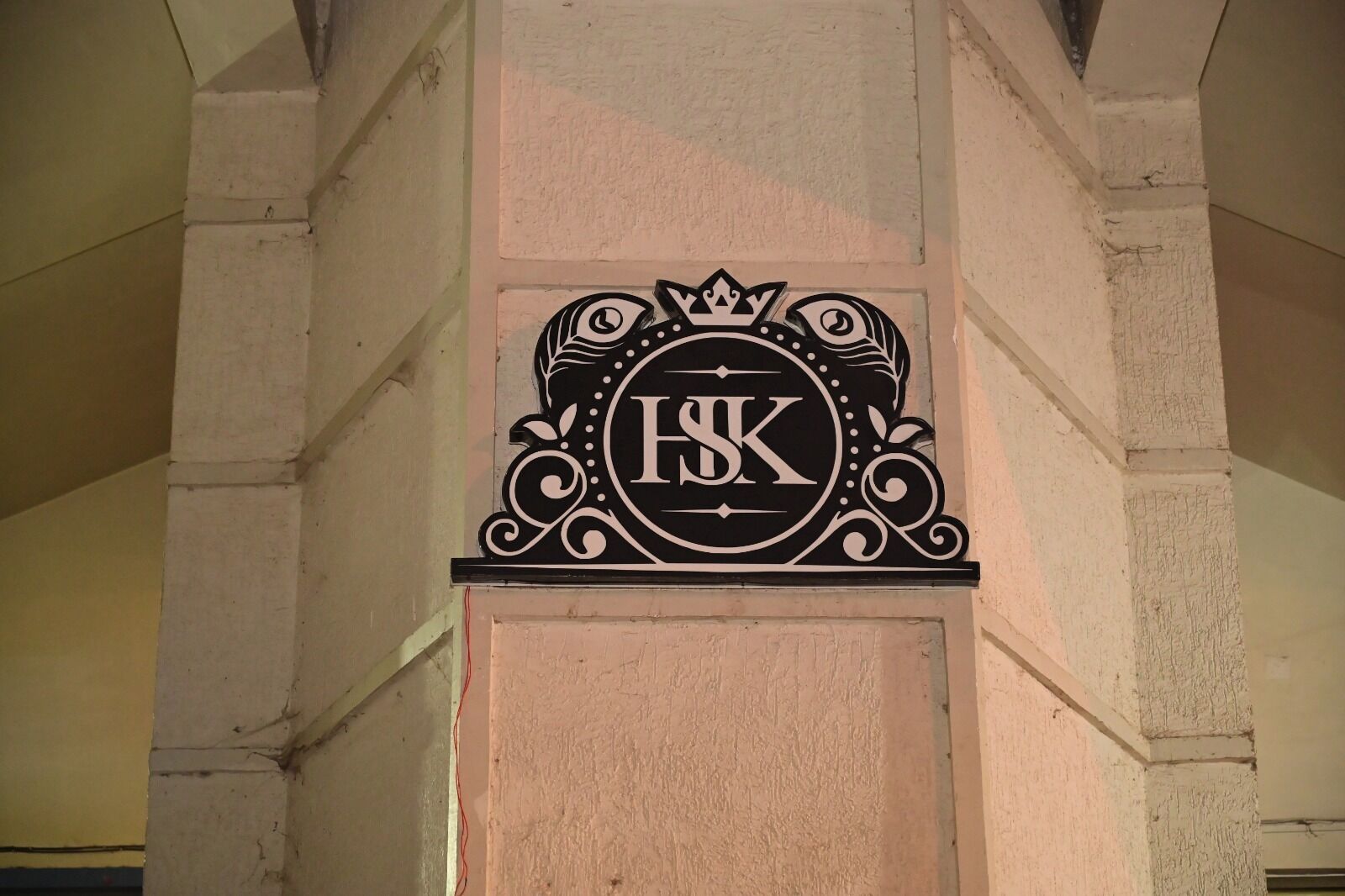 Un letrero negro con las letras 'ISK' en una tipografía decorativa, sujeto a una pared beige con textura.
