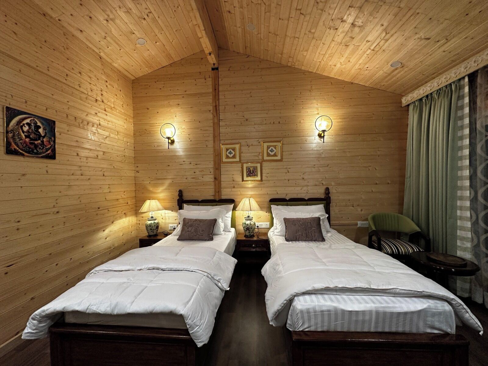 A wooden-paneled room with two beds, wall-mounted lamps, and a green chair.