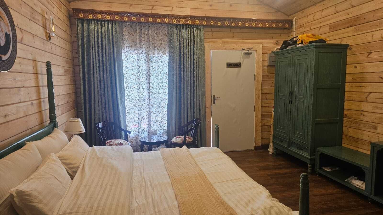A wooden room with a bed, two chairs, a table, a cabinet, and a door with a sign.