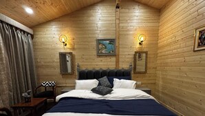 Une chambre à coucher aux murs lambrés, avec un lit, deux lampes fixées au mur et un tableau au-dessus du lit.