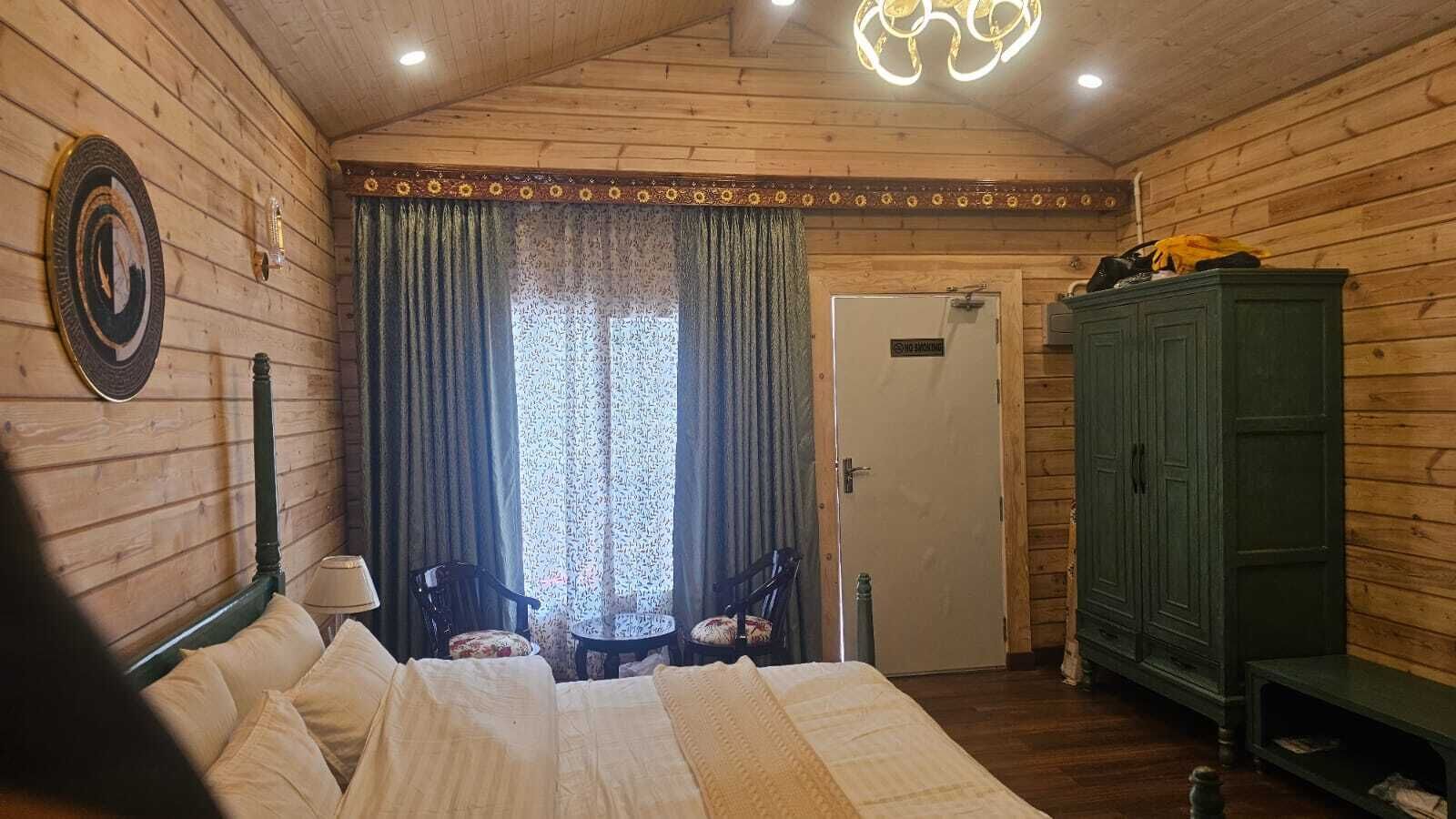 Una stanza in legno con un letto, due sedie, un armadio e una porta con il cartello 'No Smoking'.