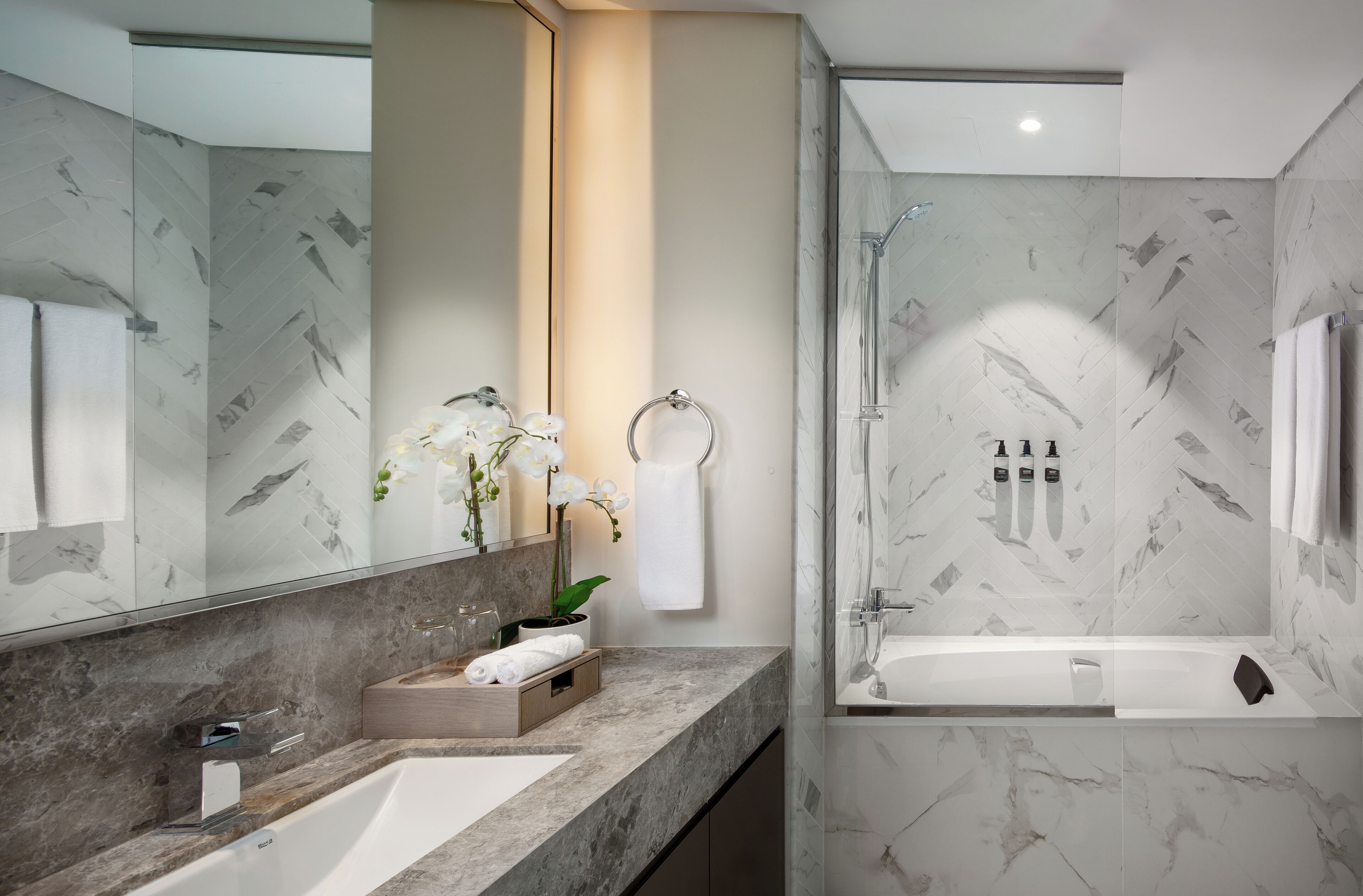 Un baño moderno con lavamanos de mármol, cabina de ducha de vidrio y un espejo grande.