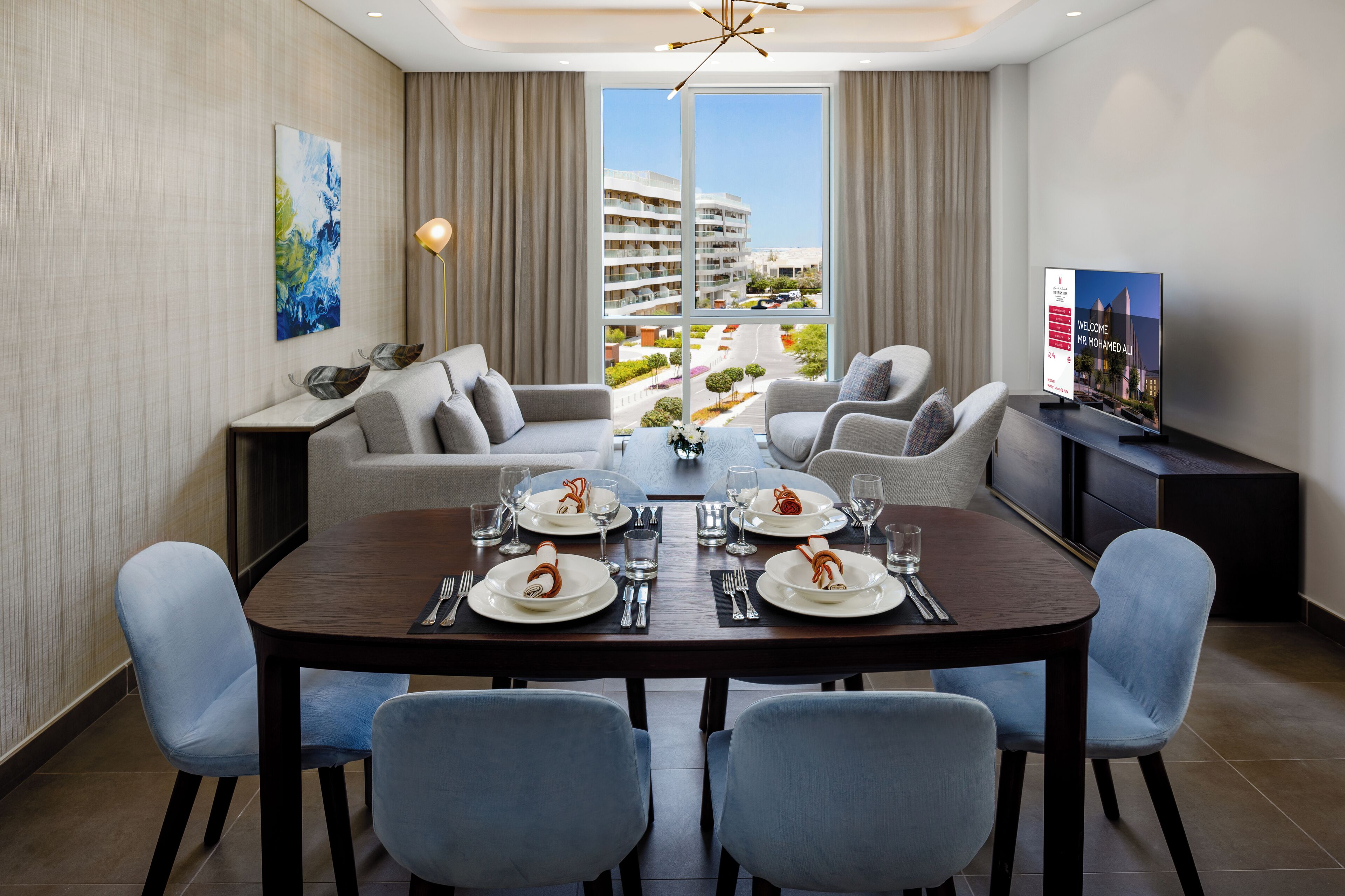 A modern dining area with a large table set for four, a sofa, and a television on a stand.