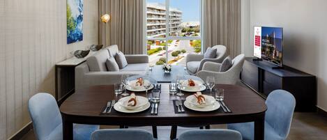 A modern dining area with a large table set for four, a sofa, and a television on a stand.