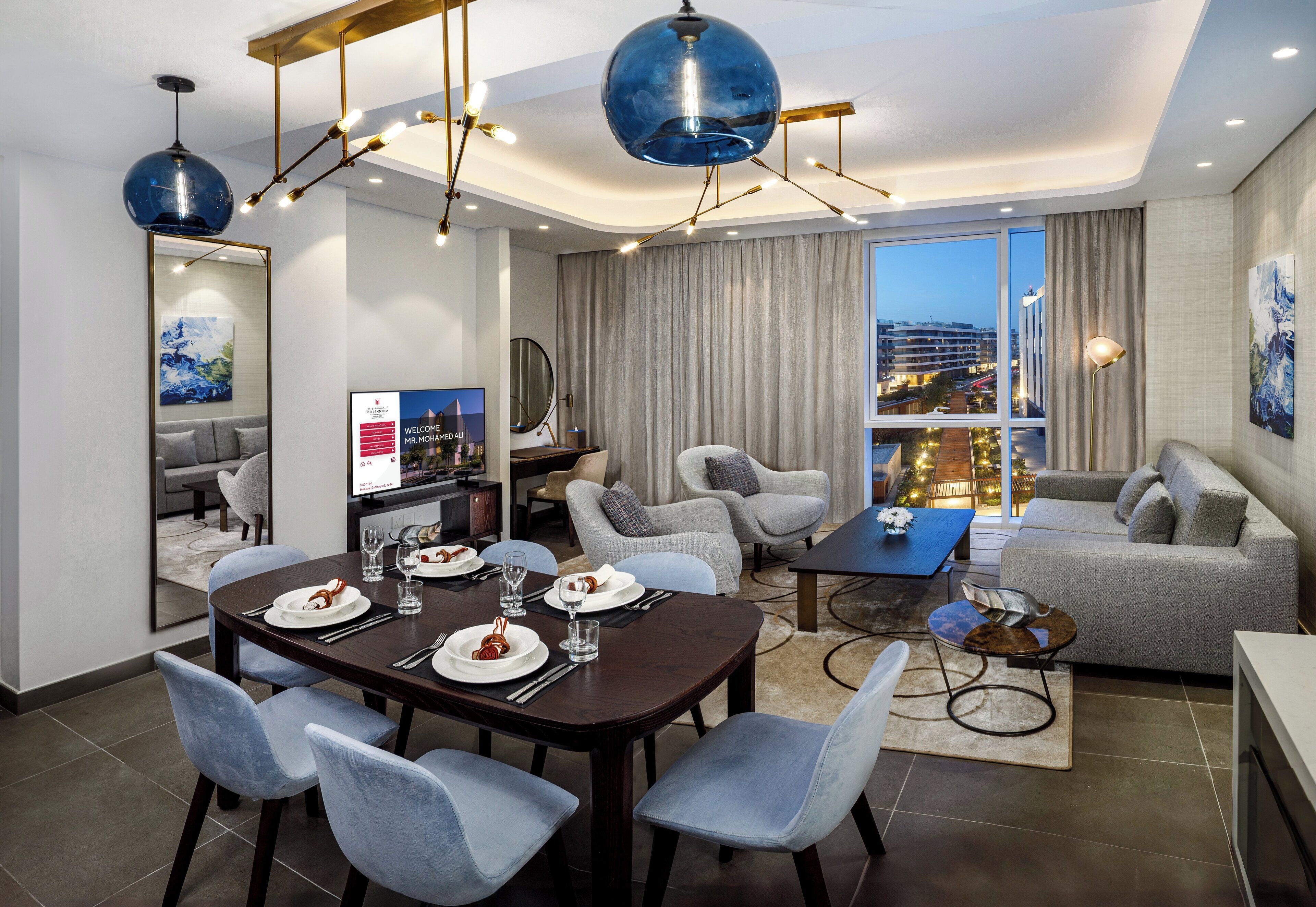 Quarto de hotel moderno com área de refeições, assentos e uma grande janela com vista para a cidade.
