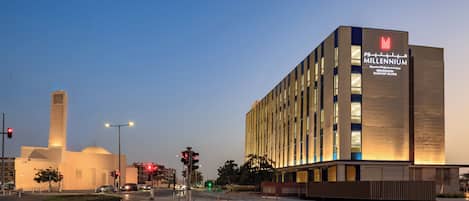 Un bâtiment moderne, orné d’une grande enseigne « Millennium », se distinguant par son design épuré et rectangulaire, avec des lignes verticales et des fenêtres illuminées.