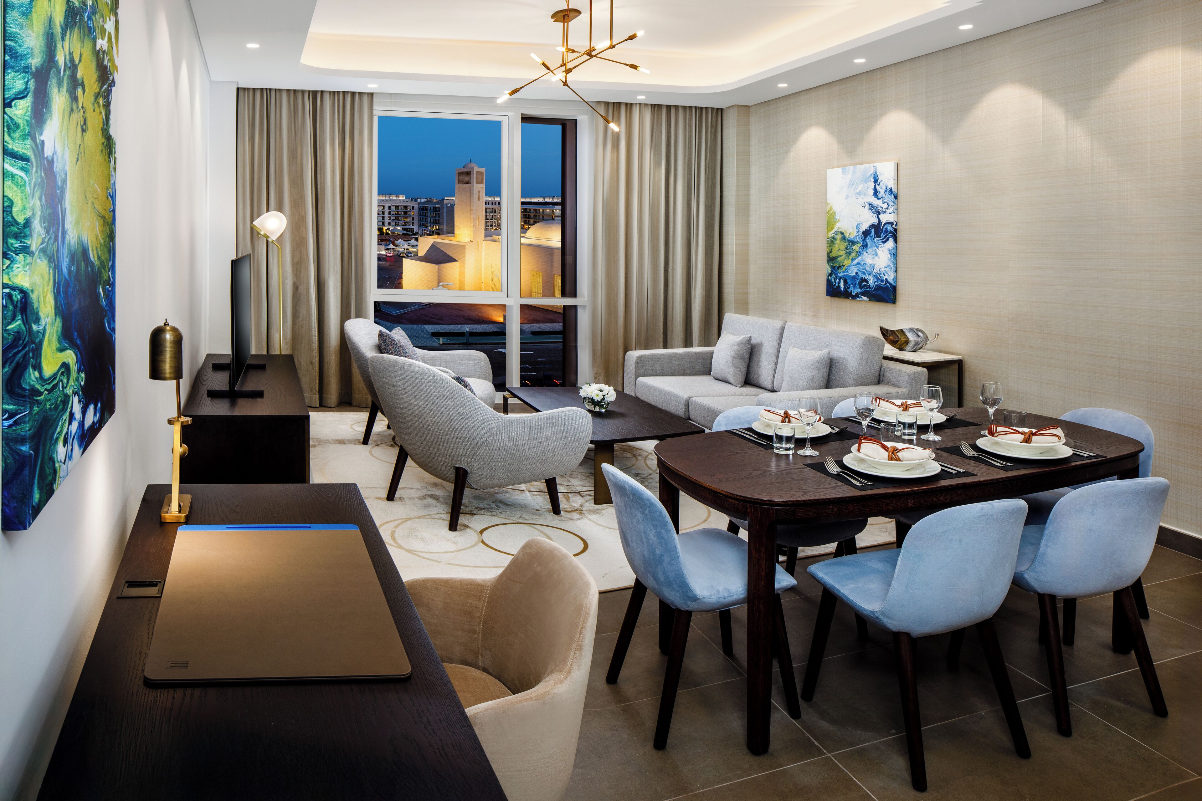 A modern hotel room with a dining area, a sofa set, and a city view.
