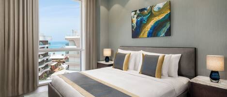 A hotel room with a large bed, two bedside tables, a nightstand, a window with curtains, and a painting on the wall.