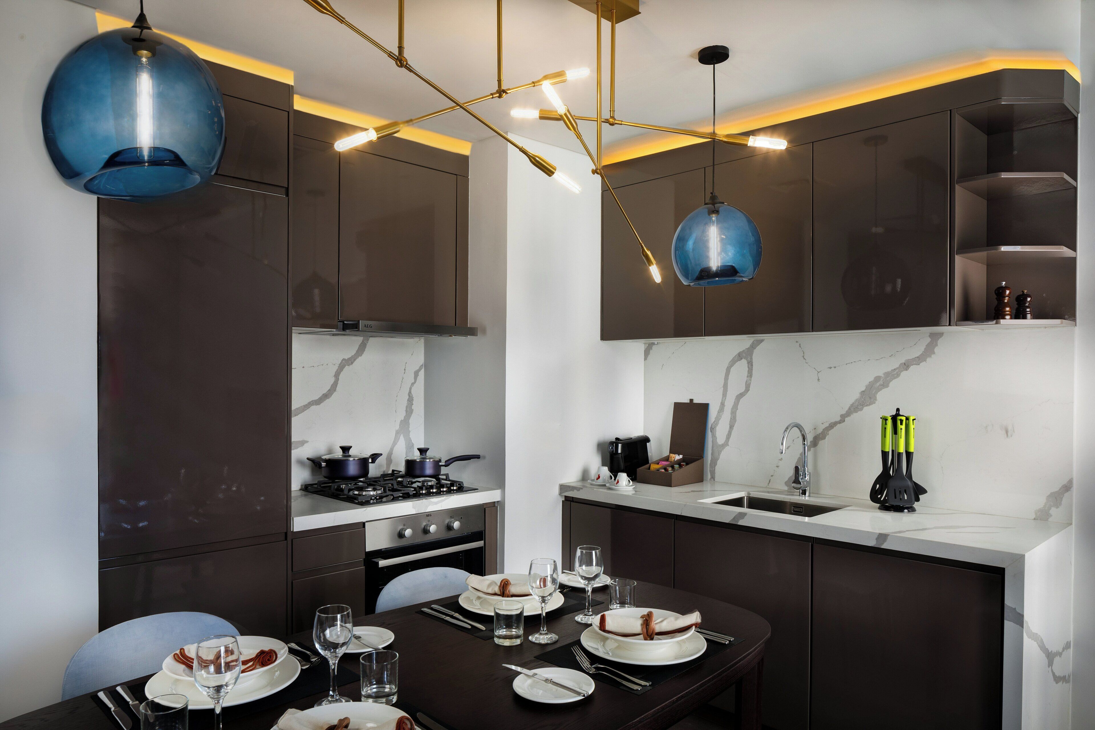 A modern kitchen with dark cabinetry, a marble countertop, and contemporary lighting fixtures.
