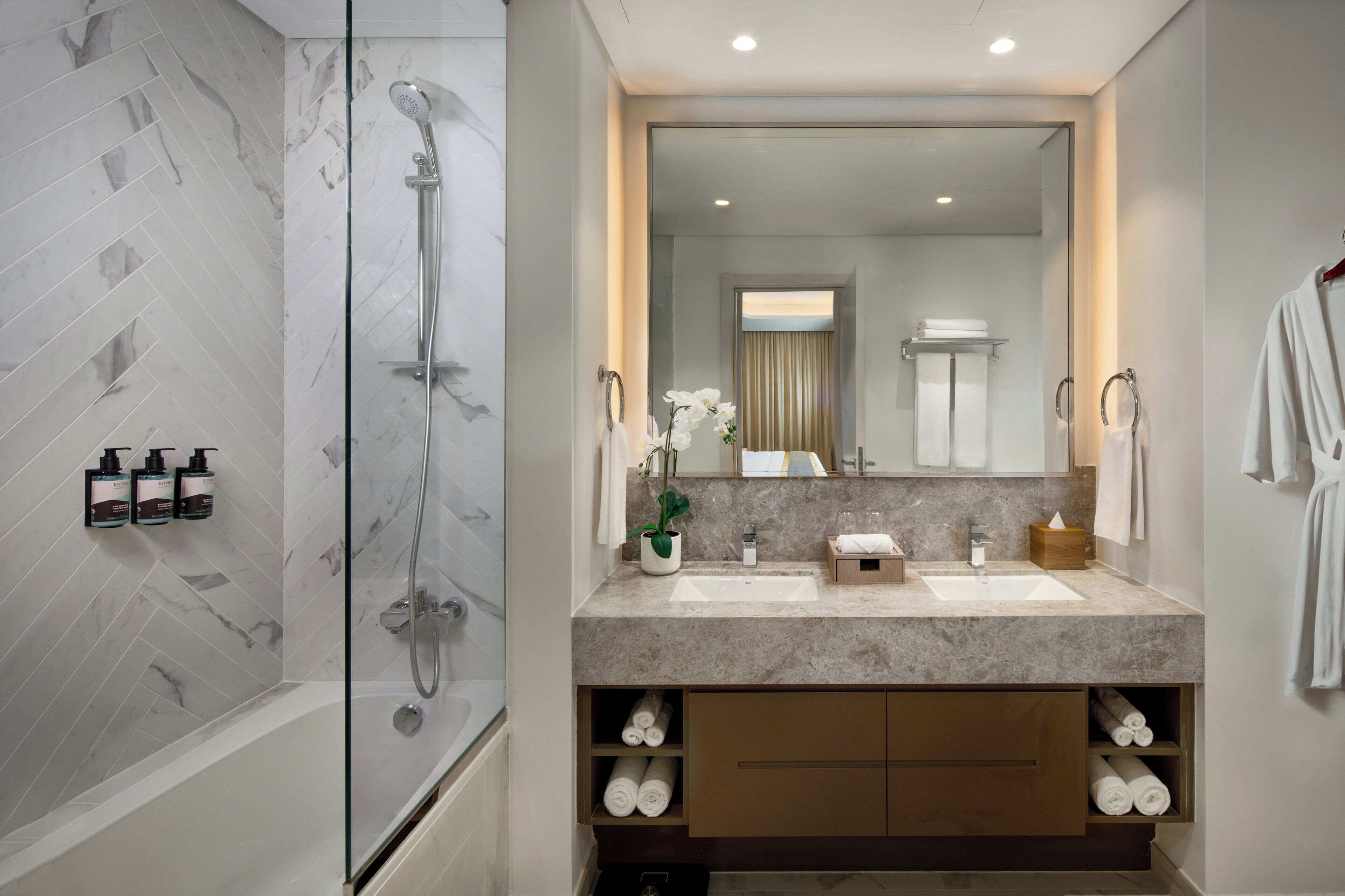 A modern bathroom with a glass-enclosed shower, two sinks, a large mirror, and a vanity with storage.