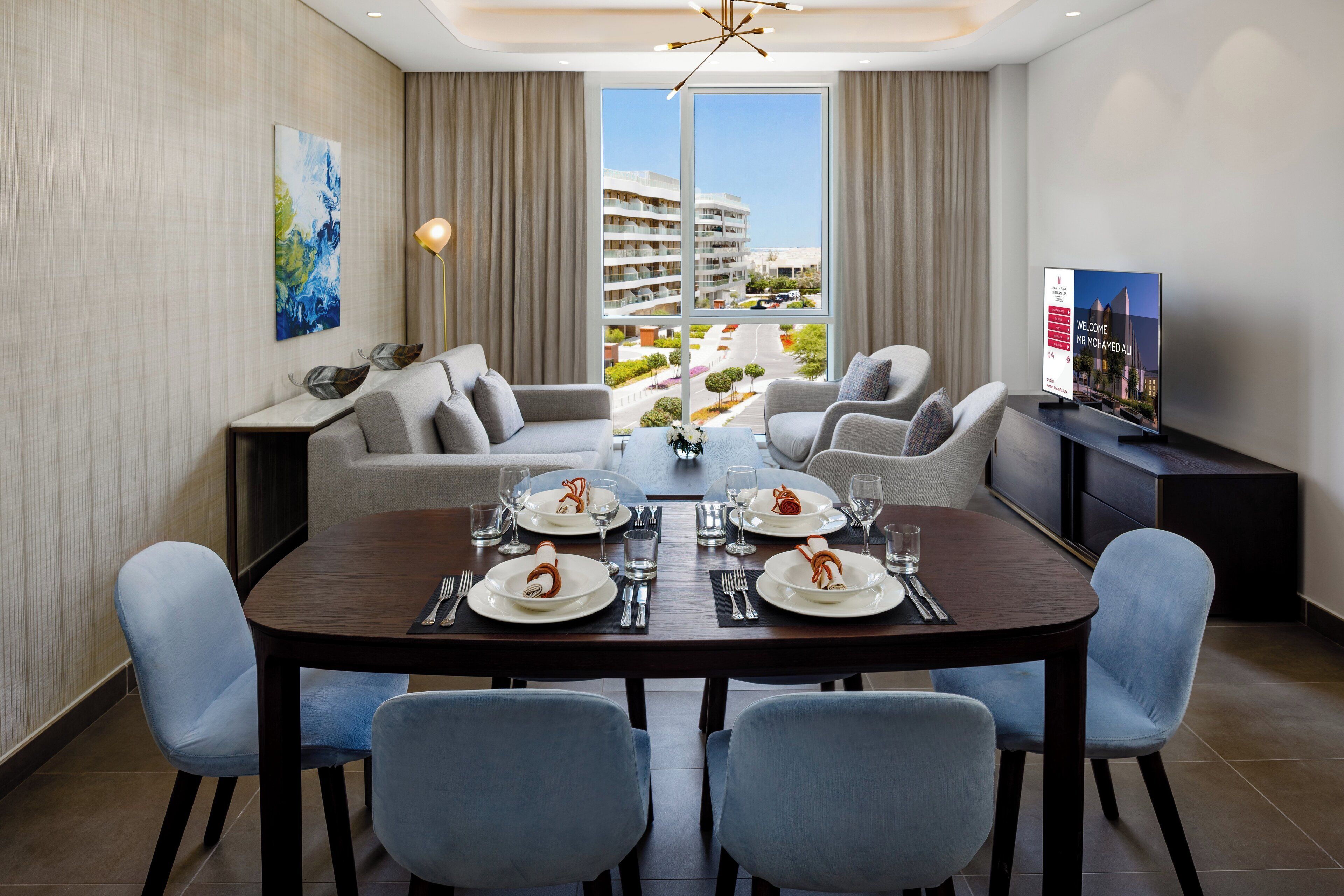A modern dining area with a large table set for four, a sofa, and a television on a stand.