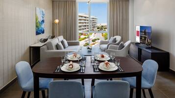 A modern dining area with a large table set for four, a sofa, and a television on a stand.