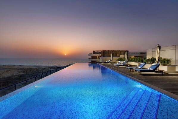 Ein Pool mit Sonnenuntergangsblick, Liegestühlen und einer Holzterrasse.