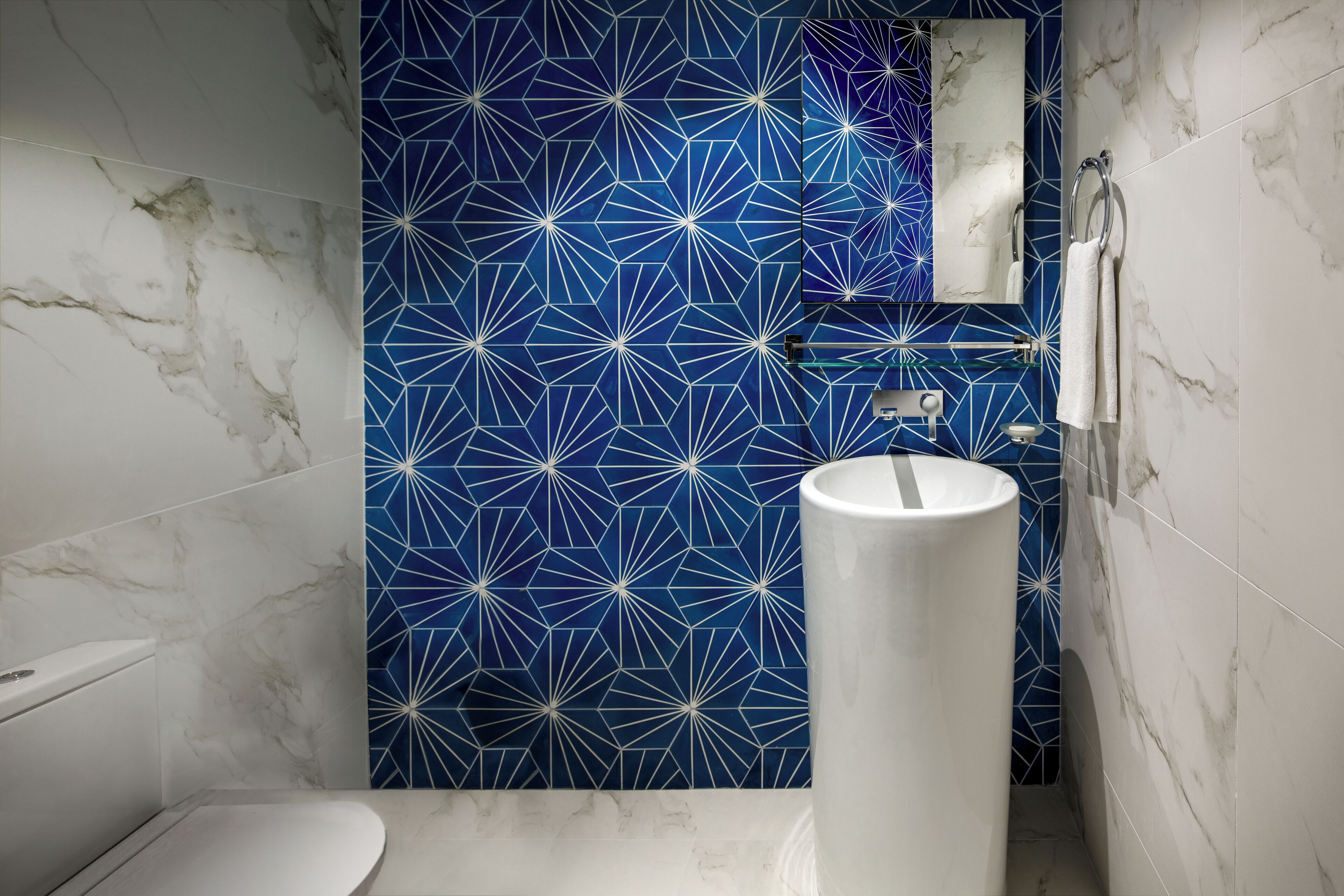 A bathroom with a white toilet, a white sink, and a blue geometric-patterned wall.