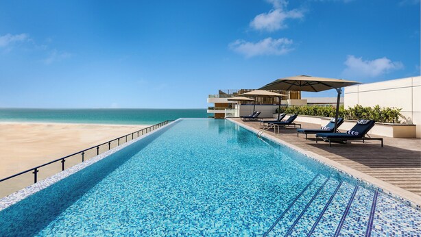 Ein Swimmingpool mit Blick auf den Strand, Liegestühle und eine überdachte Sitzgelegenheit.