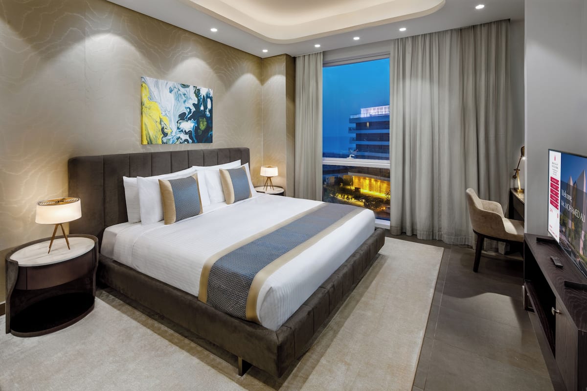 Una habitación de hotel moderna con una cama grande, vistas de la ciudad y un escritorio con televisor.