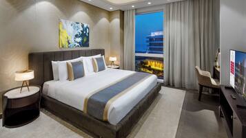 A modern hotel room with a large bed, a view of the city, and a desk with a television.