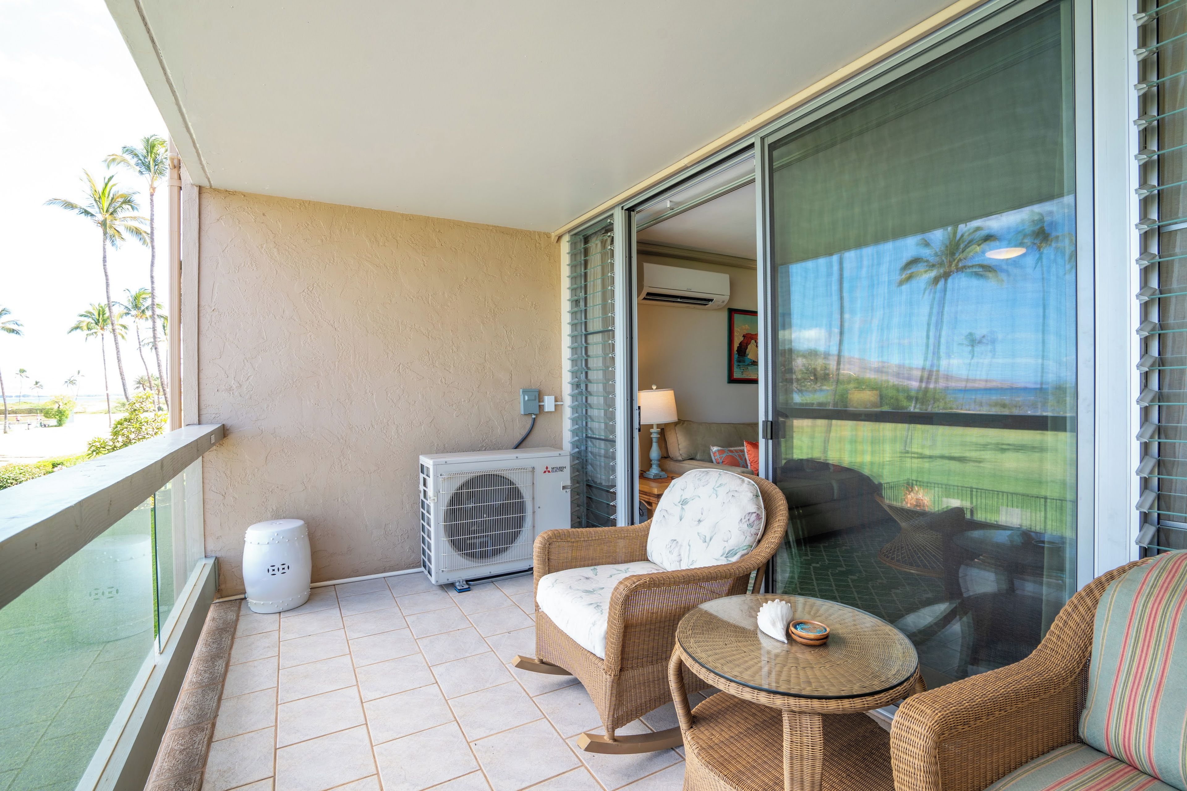 A balcony with wicker furniture, an air conditioning unit, and a view of palm trees.