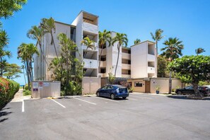 Un immeuble à plusieurs étages avec un parking, des palmiers et un ciel bleu dégagé.
