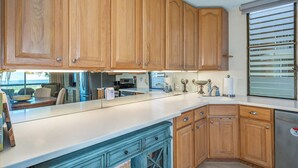 A kitchen with wooden cabinets, a white countertop, and a window with blinds.