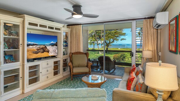 A living room with a television, wicker furniture, a glass coffee table, and a view of the ocean.