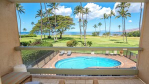 A balcony with a view of a swimming pool, palm trees, and a grassy area.