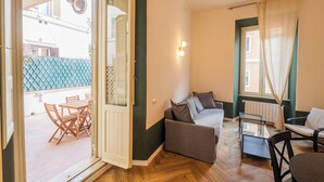 Un salon comprenant un canapé, des fauteuils, une table basse en verre et donnant sur l’extérieur.