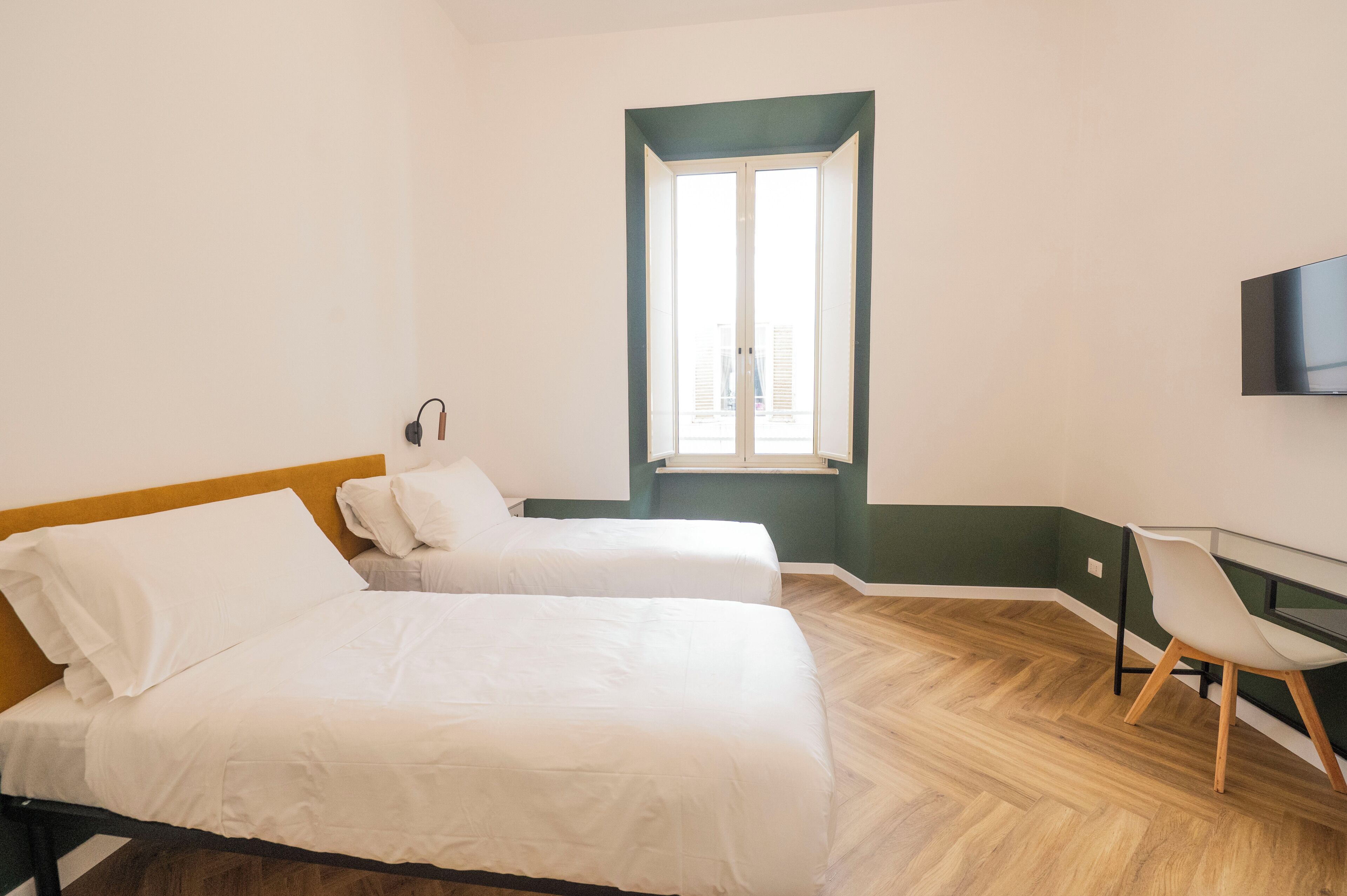 Een kamer met twee bedden, een bureau, een stoel en een televisie aan de muur.