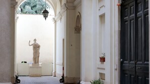 Un couloir orné d’une statue, de colonnes et d’une porte noire.