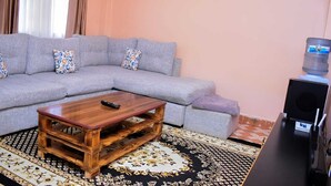 A living room with a grey sectional sofa, a wooden coffee table, a patterned rug, and a water dispenser.