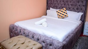 A neatly made bed with a tufted headboard, a matching ottoman, and a pillow with a geometric pattern.