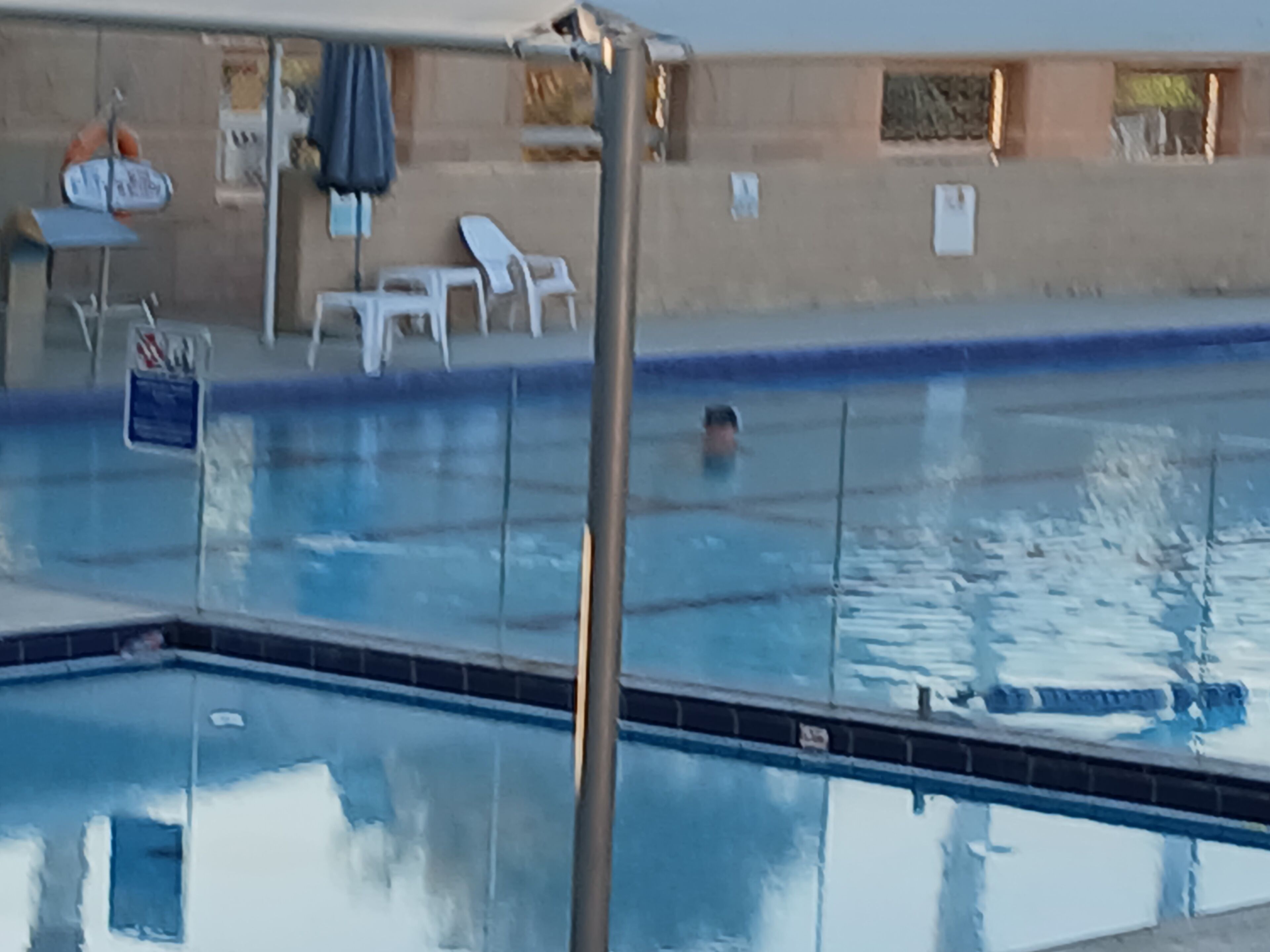 Una piscina con trampolín, sillas de descanso y un asiento para salvavidas.