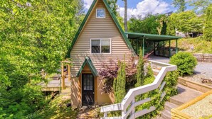 A small house with a green roof, surrounded by lush greenery and a covered porch.