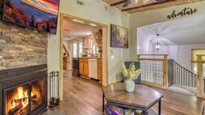 A spacious living area with a fireplace, wooden flooring, a dining table, and a kitchen in the background.
