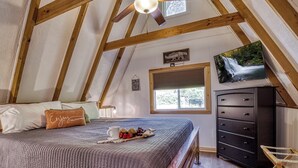An attic bedroom with a bed, a dresser, a television, and a window.